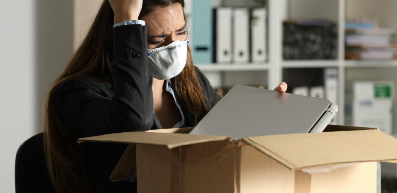 Gefeuerte Managerin mit Schutzmaske, die persönliche Gegenstände in eine Kiste im Büro packt
