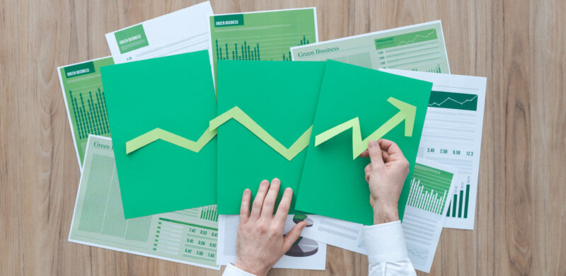 Geschäftsmann, der ein erfolgreiches Finanzdiagramm mit grünem Papierpfeil nach oben auf dunkelgrünem Papier legt