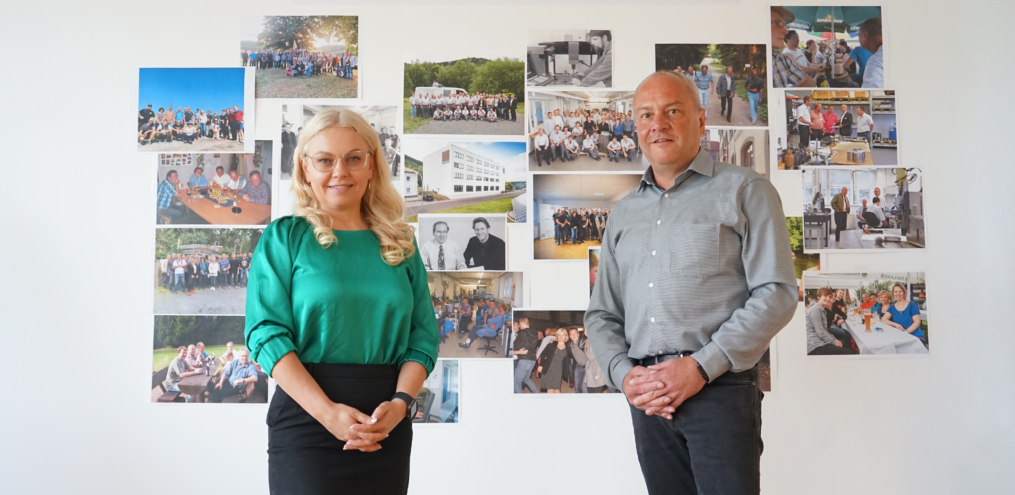 Die Geschäftsführer der Werkzeugbau Ruhla GmbH, Lena Lüneburger und Udo Köllner, vor der Fotowand des Unternehmens zum diesjährigen 30-jährigen Firmenjubiläum.