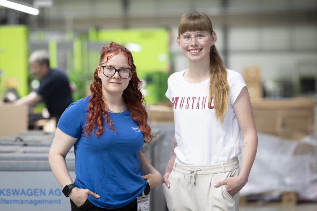 Zwei junge Frauen stehen nebeneinander und lächeln in die Kamera.