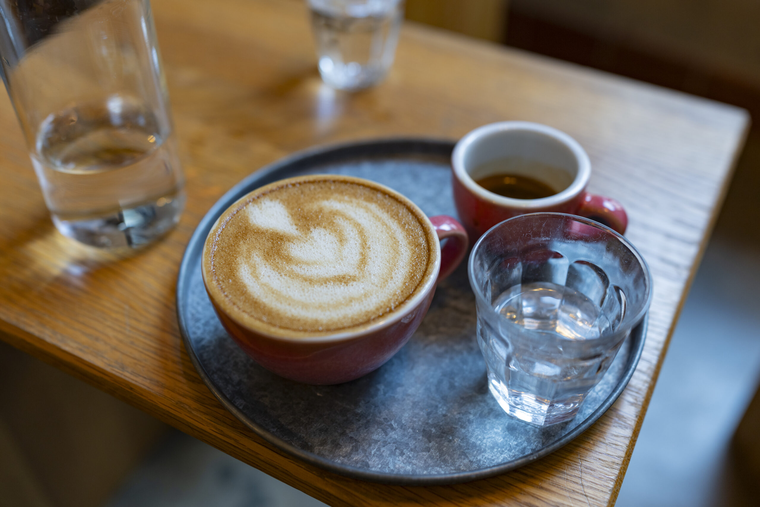 Zwei zubereitete Kaffeespezialitäten und Wassergläser stehen auf einem Holztisch