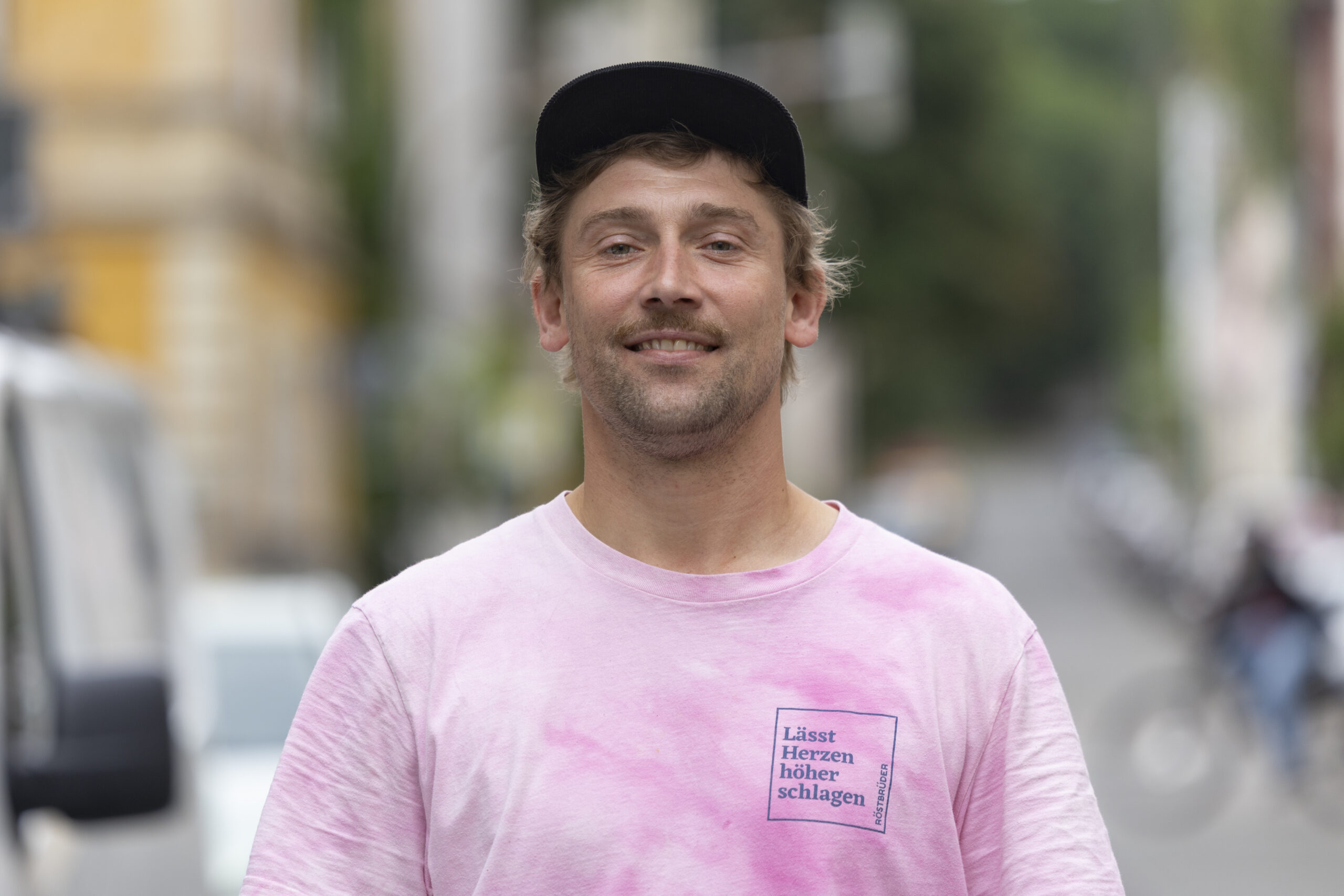 Daniel Rindermann von den Röstbrüdern steht neben gestapelten Säcken mit Rohkaffee vor der Rösterei.