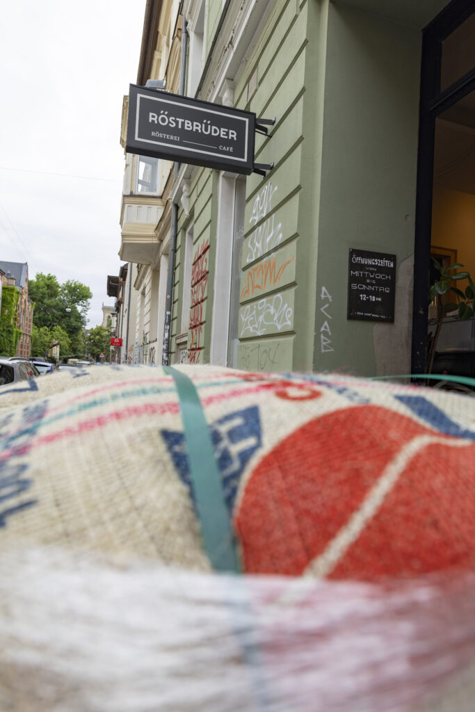 Kaffeesack im Vordergrund vor dem Firmenschild der Röstbrüder