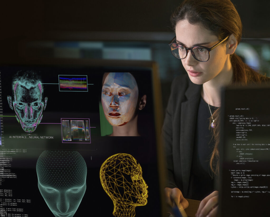 Mitarbeiterin analysiert digital dargestellte Gesichter und KI-gestützte Gesichtserkennung auf einem Bildschirm.