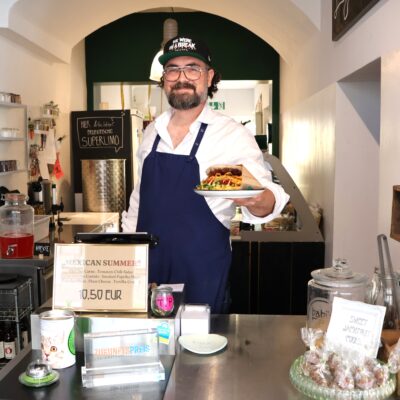 Ein Mann steht hinter der Theke und hält einen Teller mit einem Sandwich in der Hand.